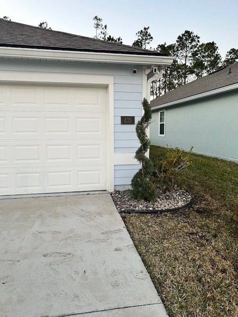 A backyard with a white rock garden bed and trimmed bushes alongside a screened-in porch.