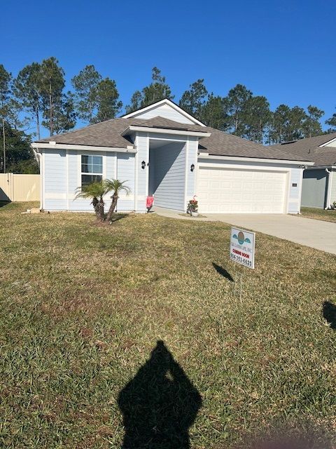 Single-story white house with a garage, front lawn, and a real estate sign in the yard.