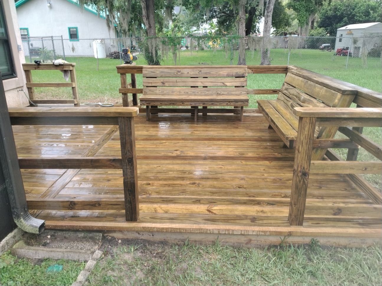 Wooden deck with built-in benches, railing, and a small table, likely in a backyard setting.