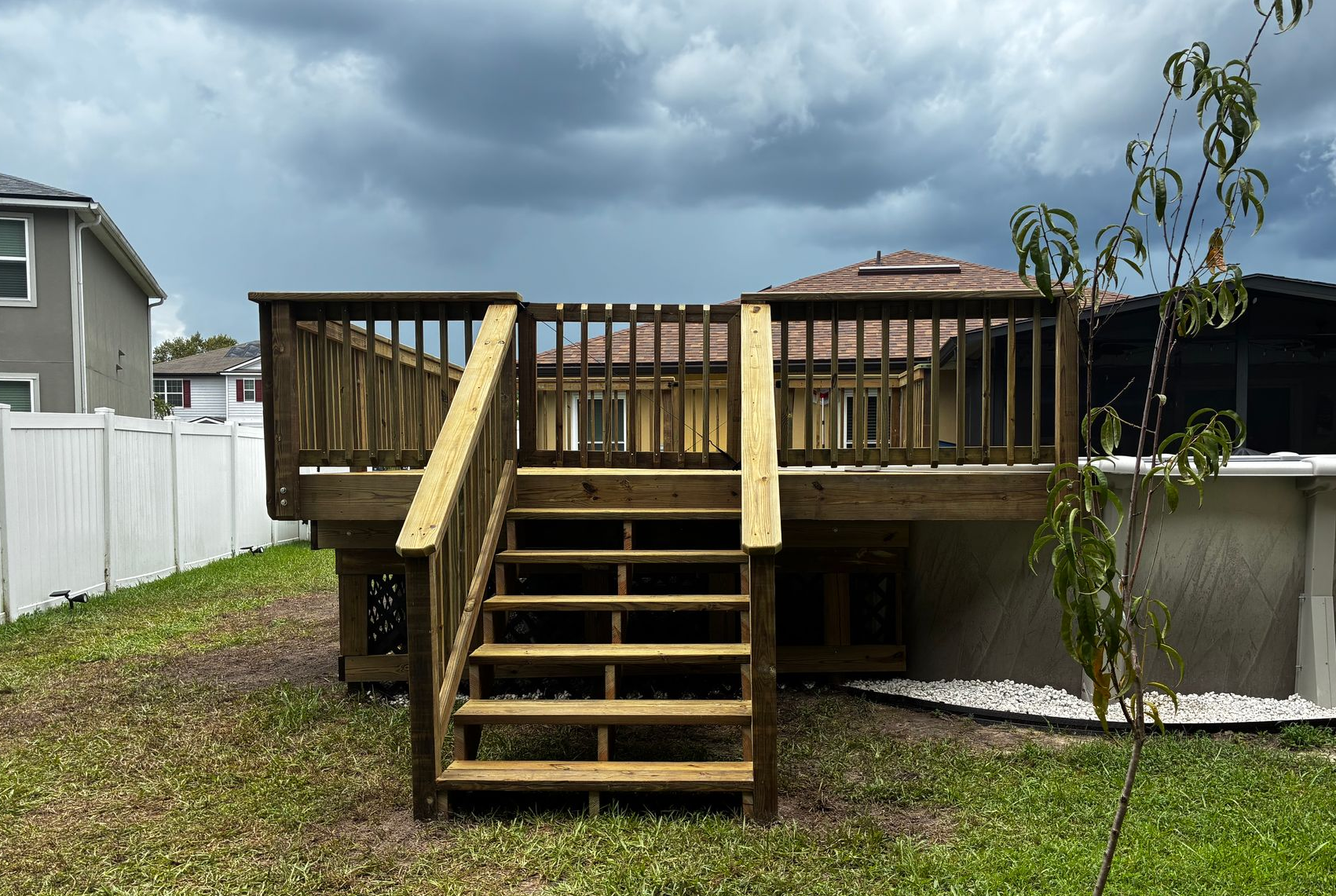 Backyard wooden deck with central stairs, white fence, and cloudy sky