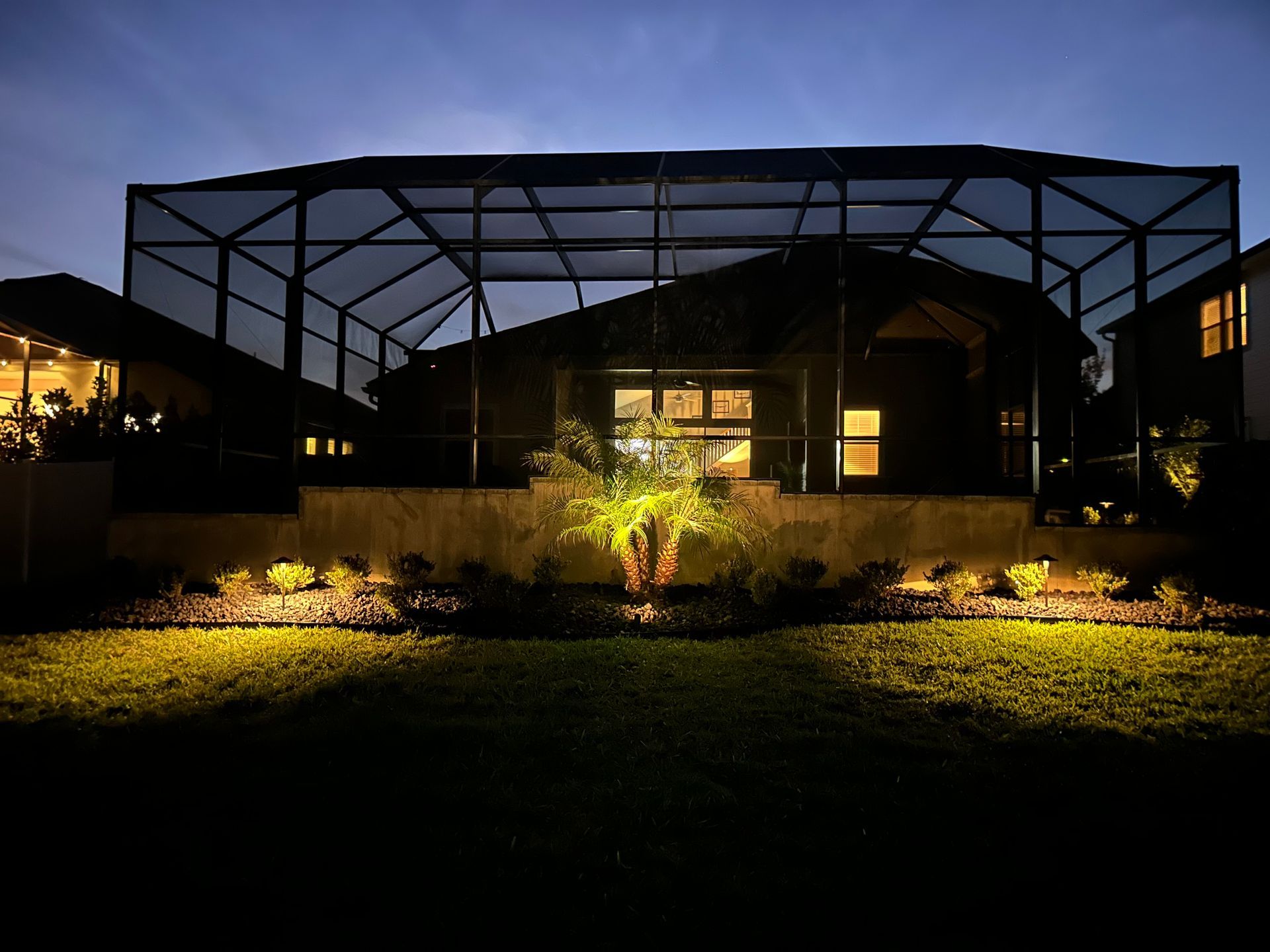 Illuminated greenhouse or pavilion at dusk with a lit garden in front