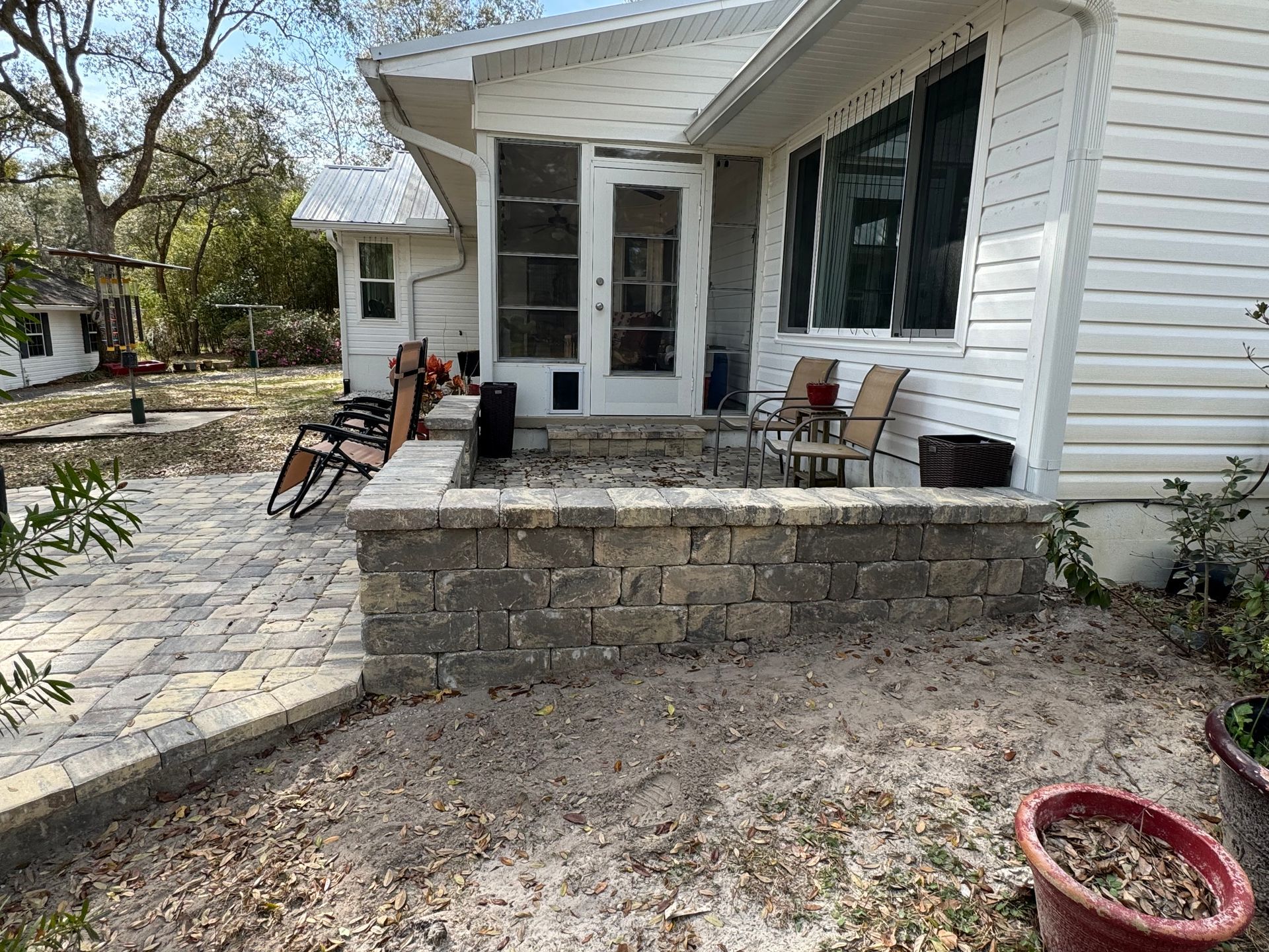 Exterior of a house with a raised brick patio. Two chairs and a small table sit on the patio.