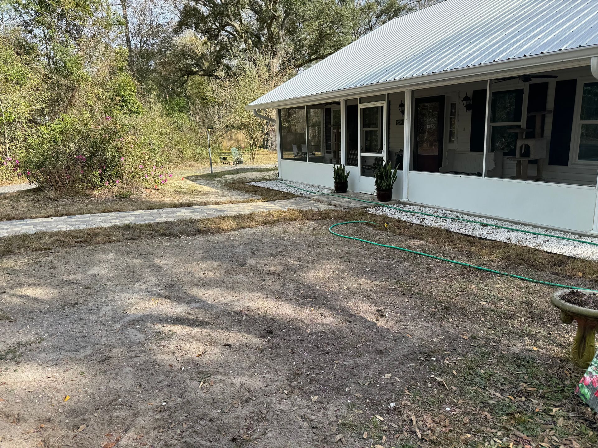 House with white trim, porch, and gravel path in a wooded setting.