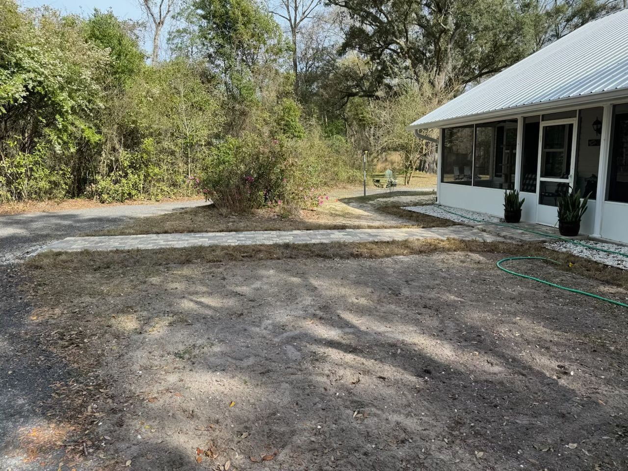 Driveway and yard with gravel border, alongside a white house with screened porch and trees.