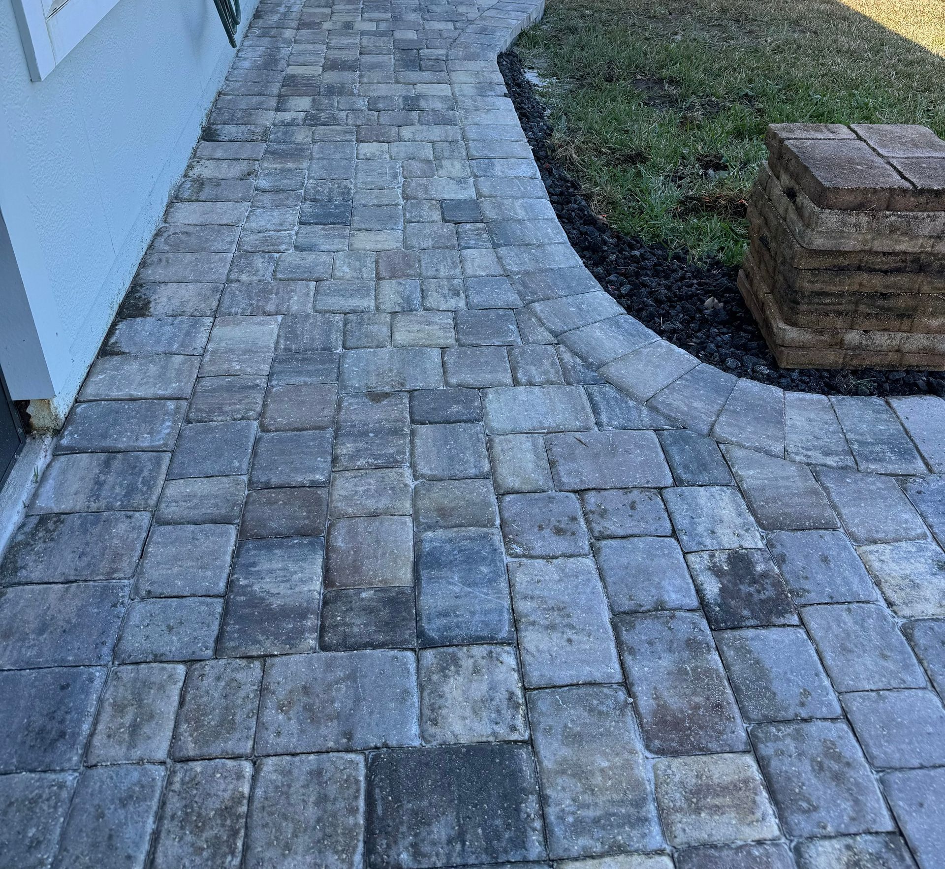 Brick pavers form a walkway alongside a light-blue building, curving toward grass.