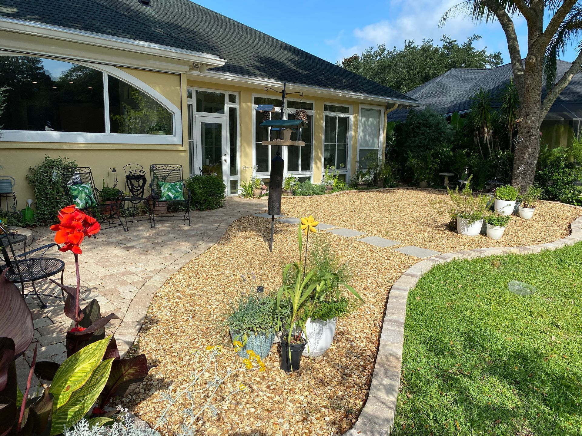 Backyard with stone ground cover, plants, bird feeder, and house.
