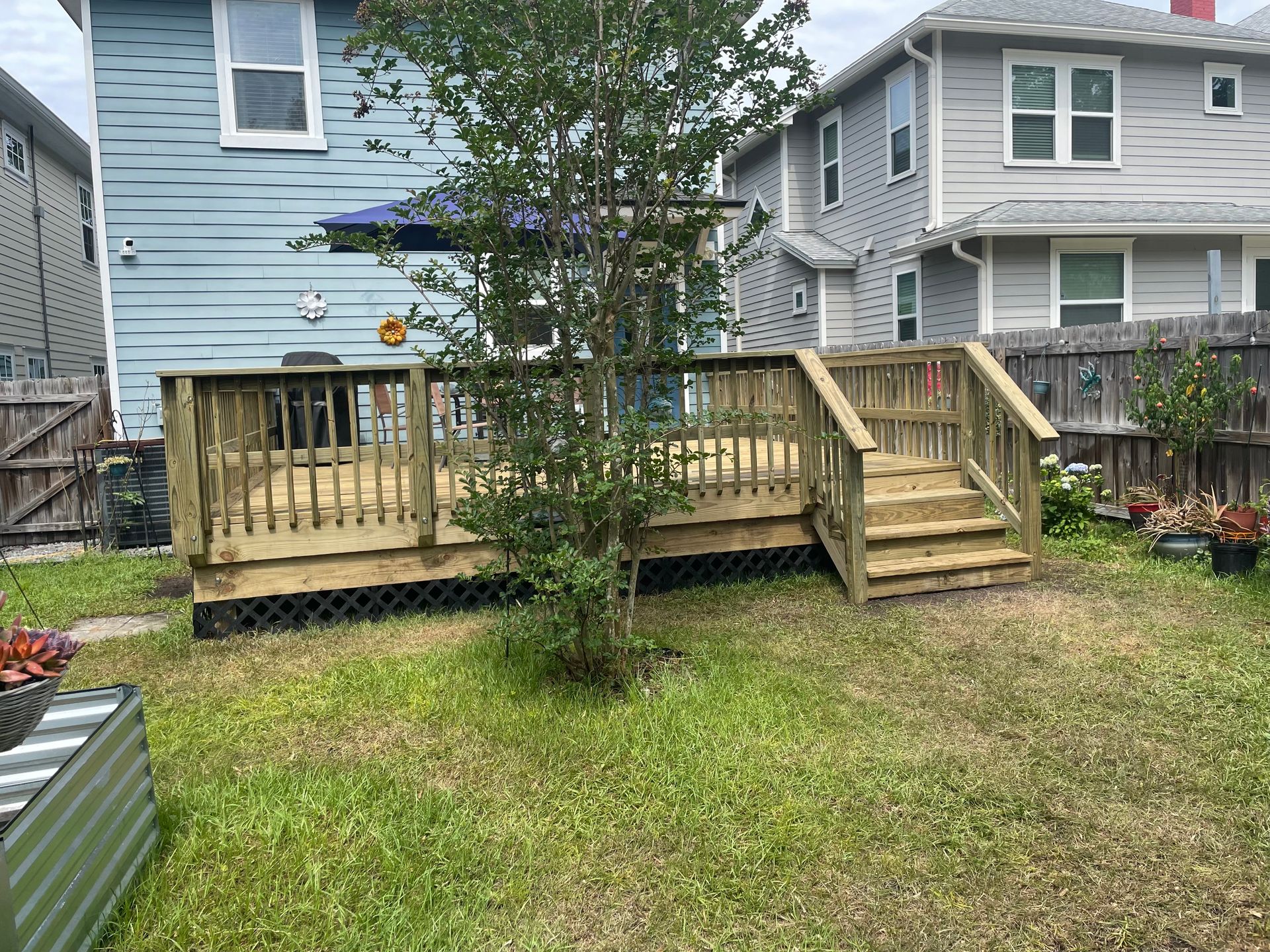 Wooden deck in a grassy backyard, connecting to a blue house with windows. Stairs lead to the deck.