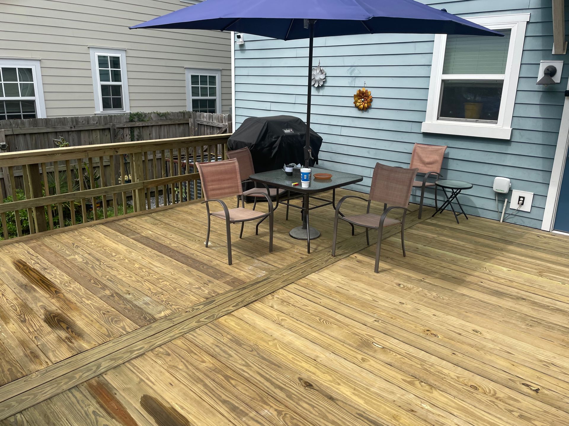 Wooden deck with table, chairs, umbrella, and grill next to a blue house.