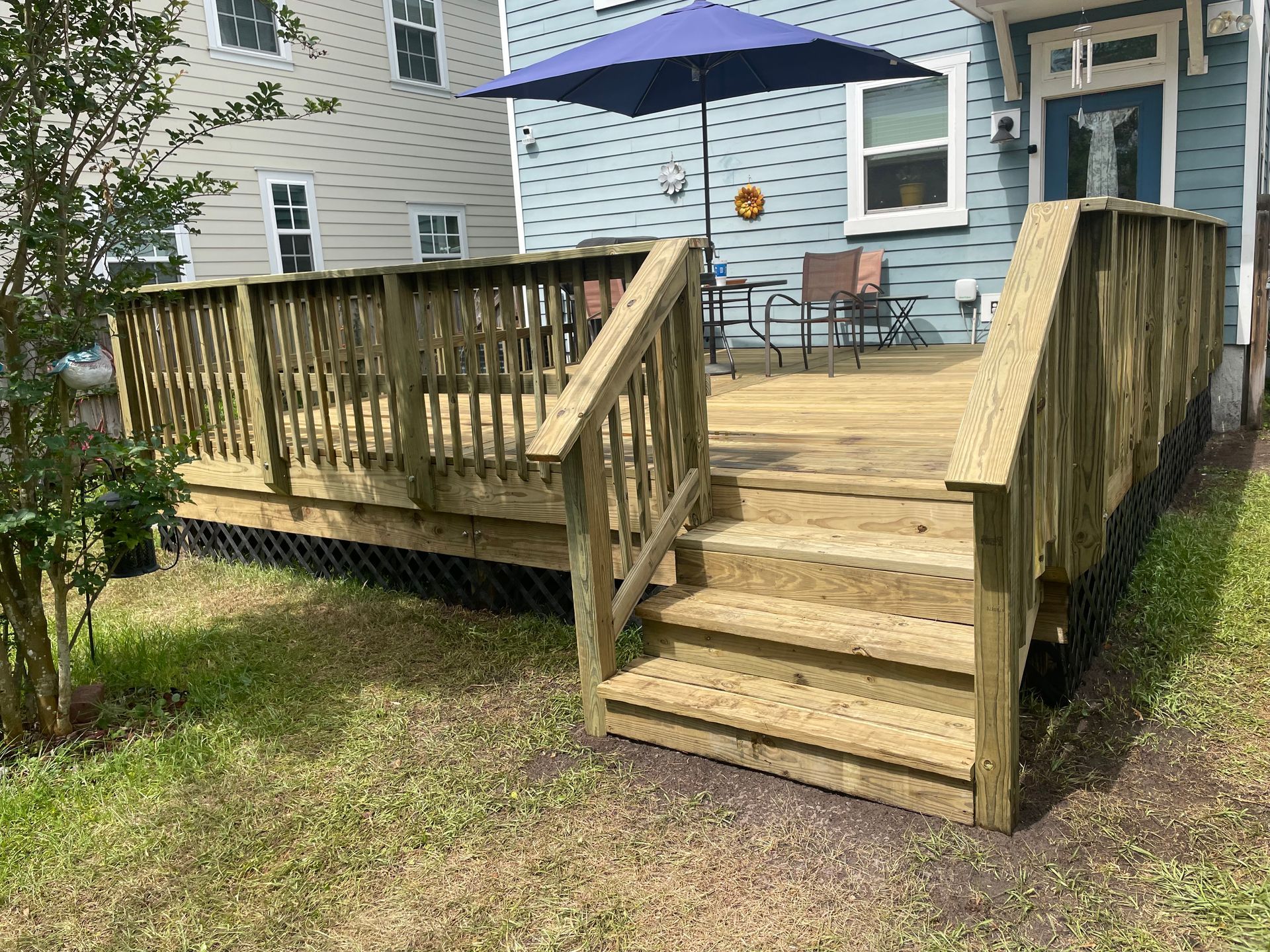 Wooden deck with steps, railing, and an umbrella over a table and chairs in a backyard.