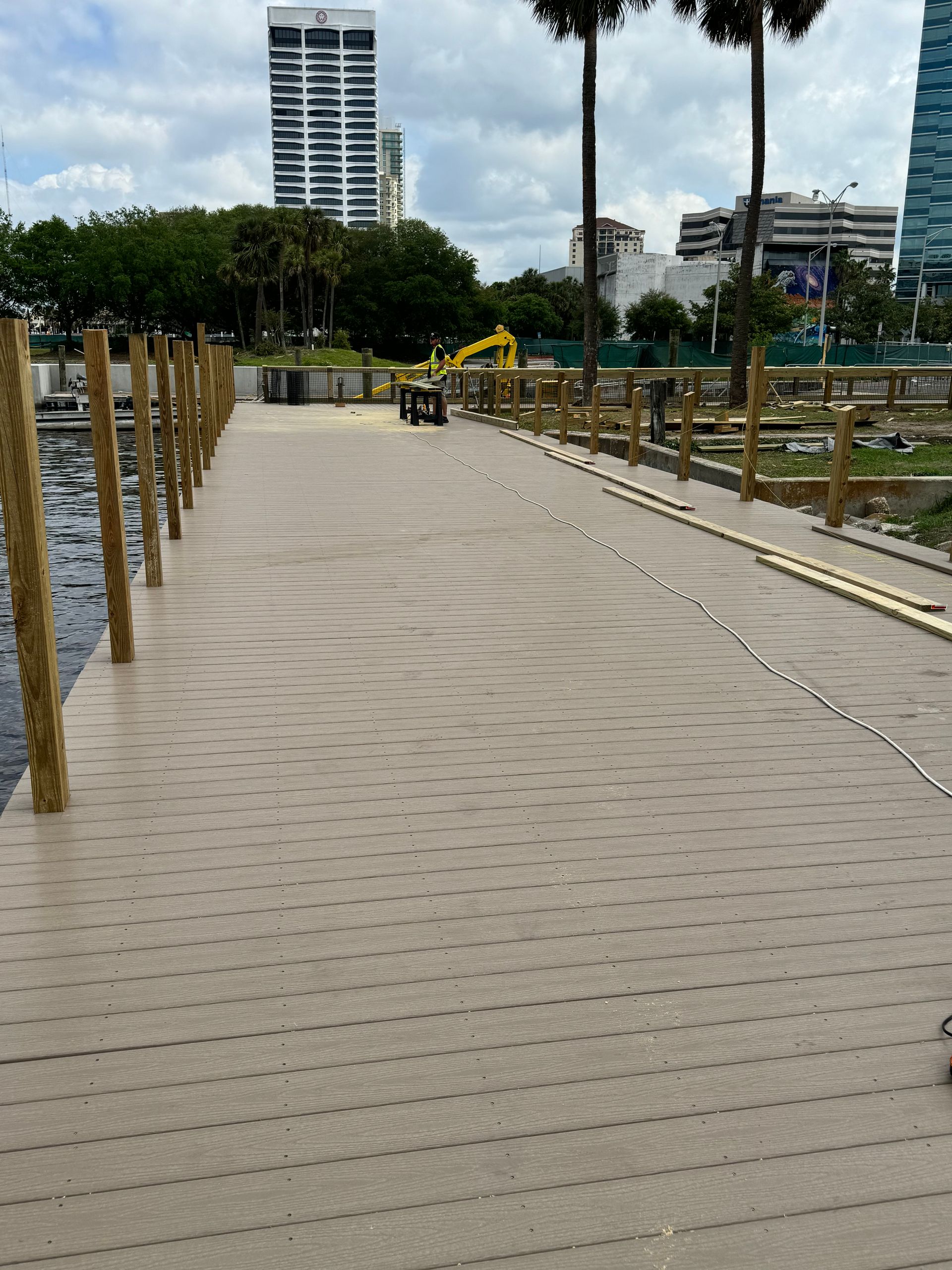 A long dock extends over water, framed by wooden posts and a city skyline.
