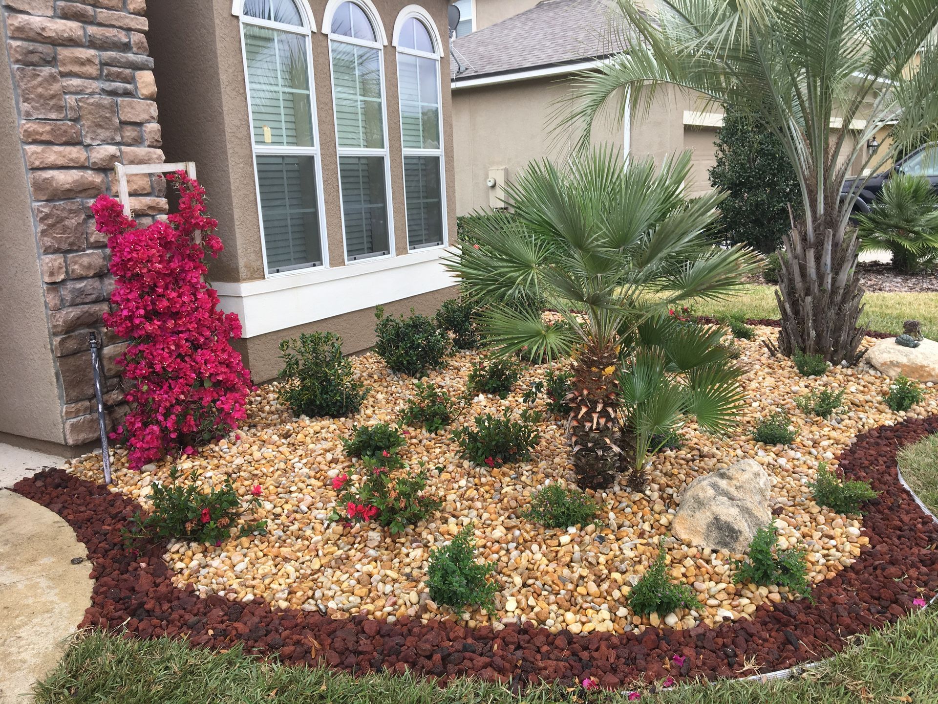 Front yard with mulch beds, trees, shrubs, and a driveway beside a house.