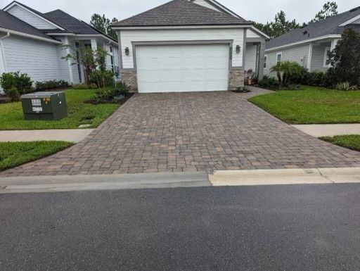 Brick driveway leading to a white garage door, with houses on either side.