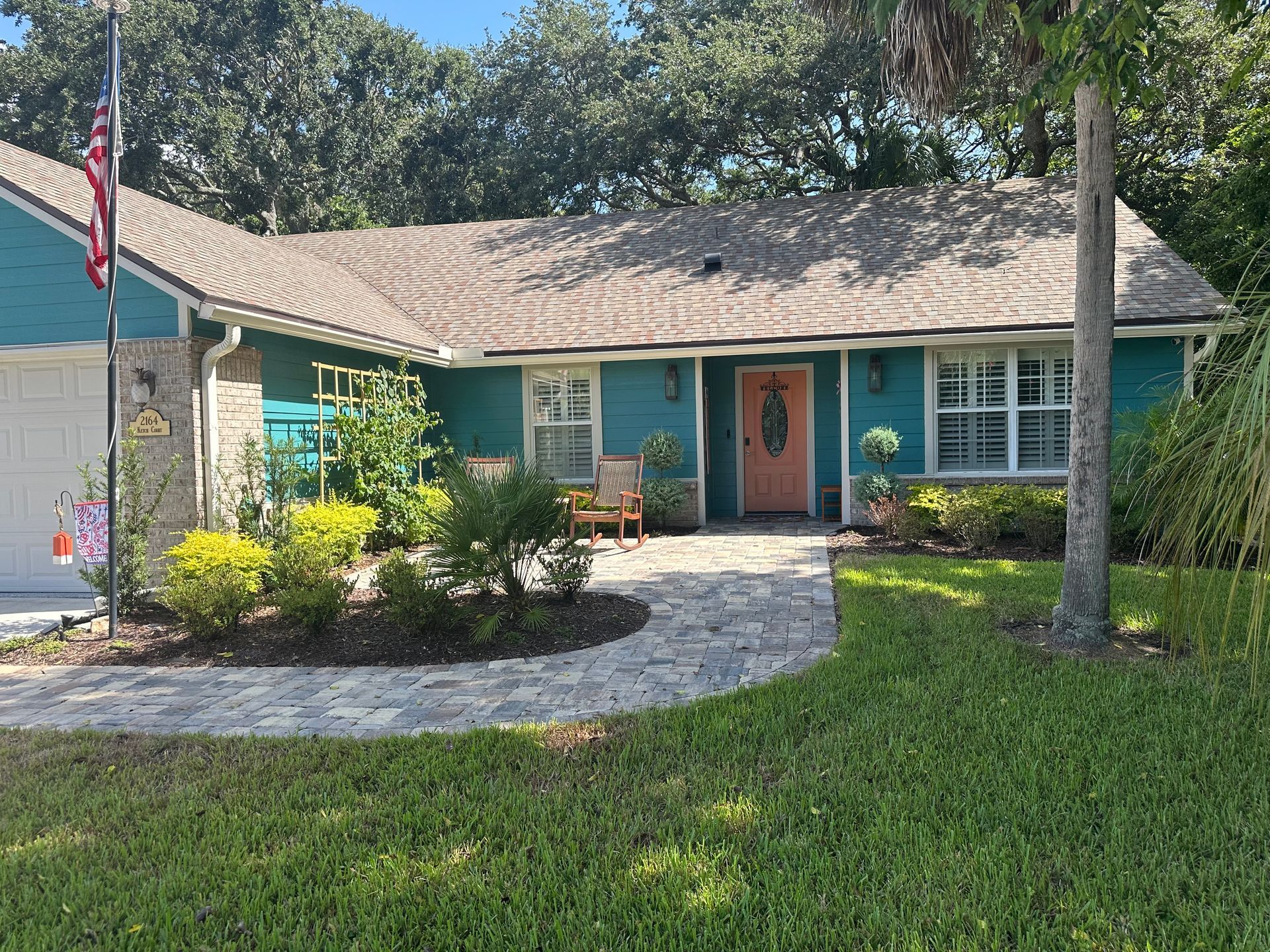 Teal-colored house with brick path. Front door is orange. American flag on left. Lush green lawn.