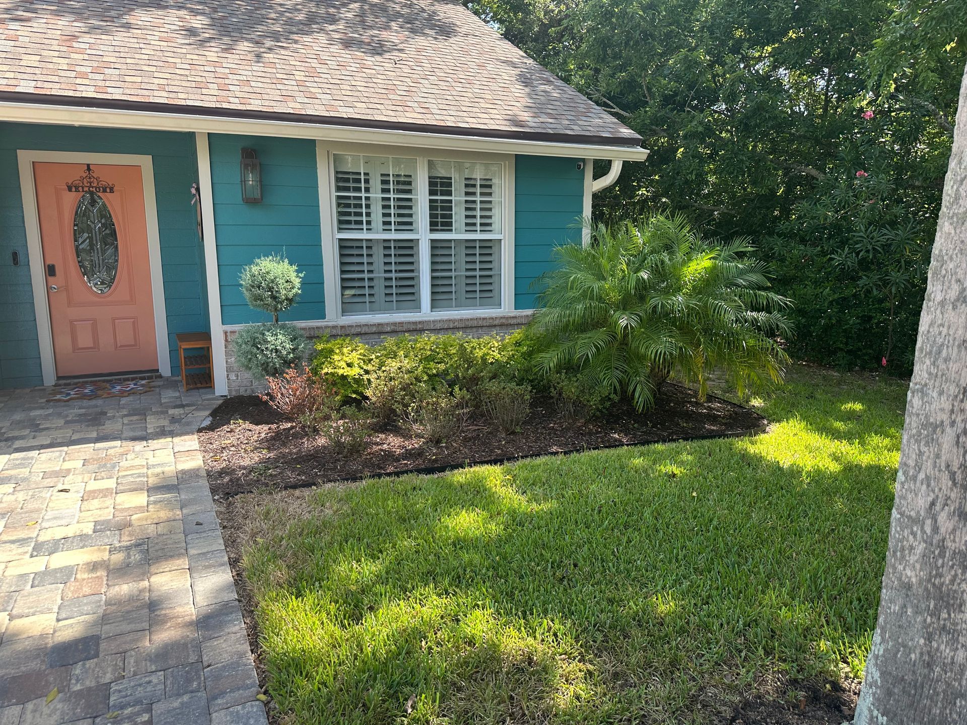 Teal house with coral door, white window, and landscaped front yard with green grass and mulch.