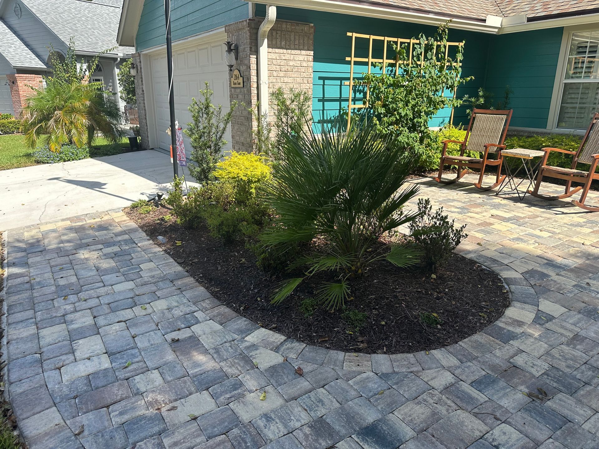 Paver walkway leading to a landscaped bed in front of a turquoise house, with rocking chairs.