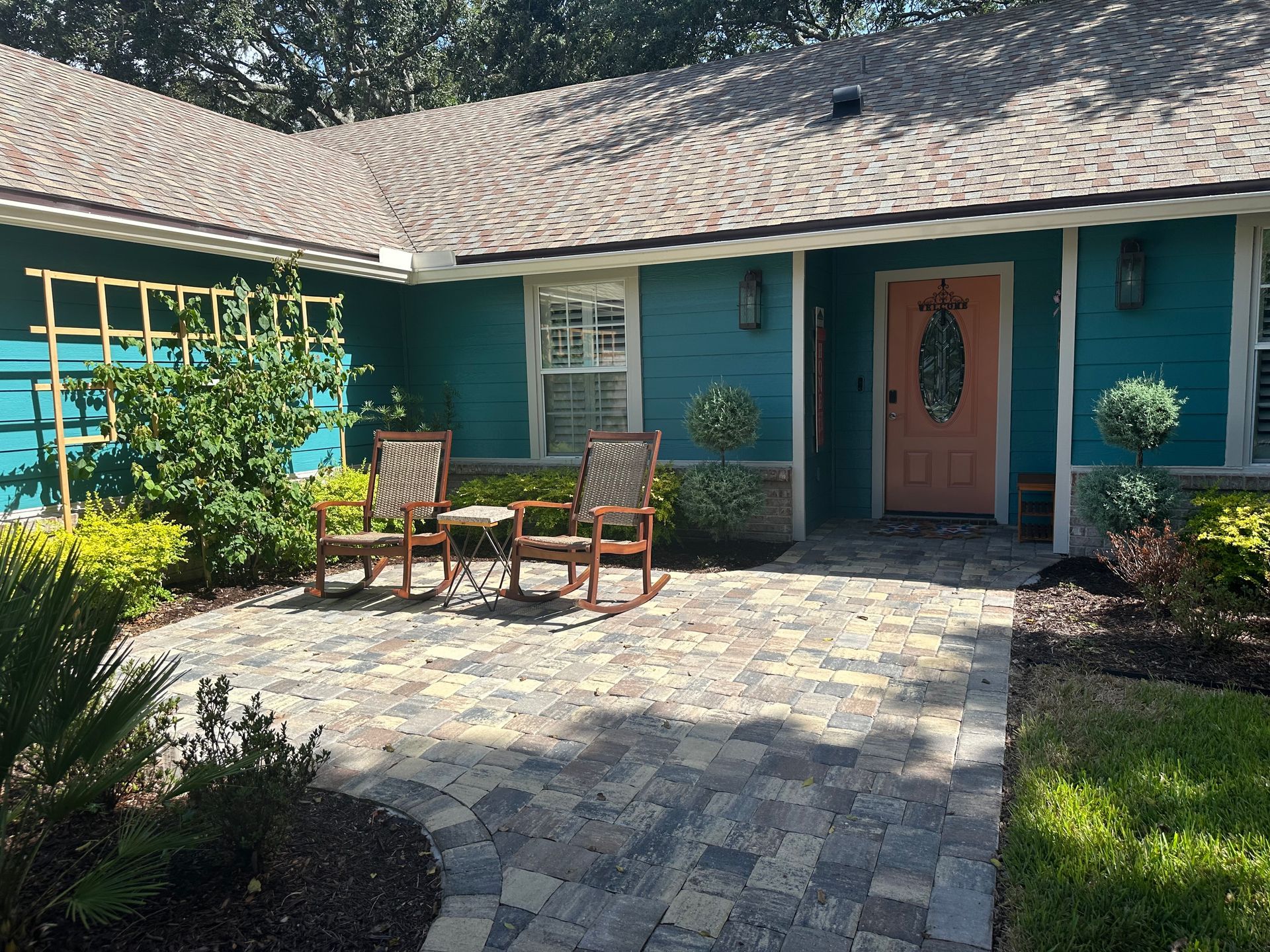 Teal house exterior with brick patio, rocking chairs, and an orange door.