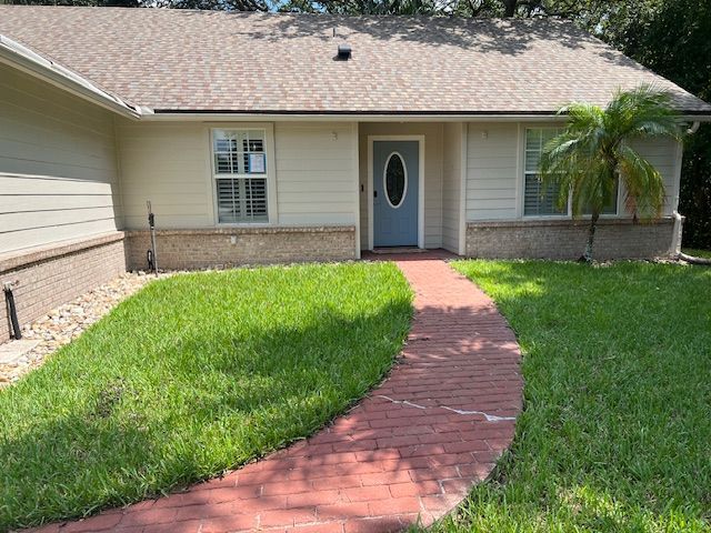 Exterior view of a house with a red brick walkway leading to a light blue door. Green lawn.