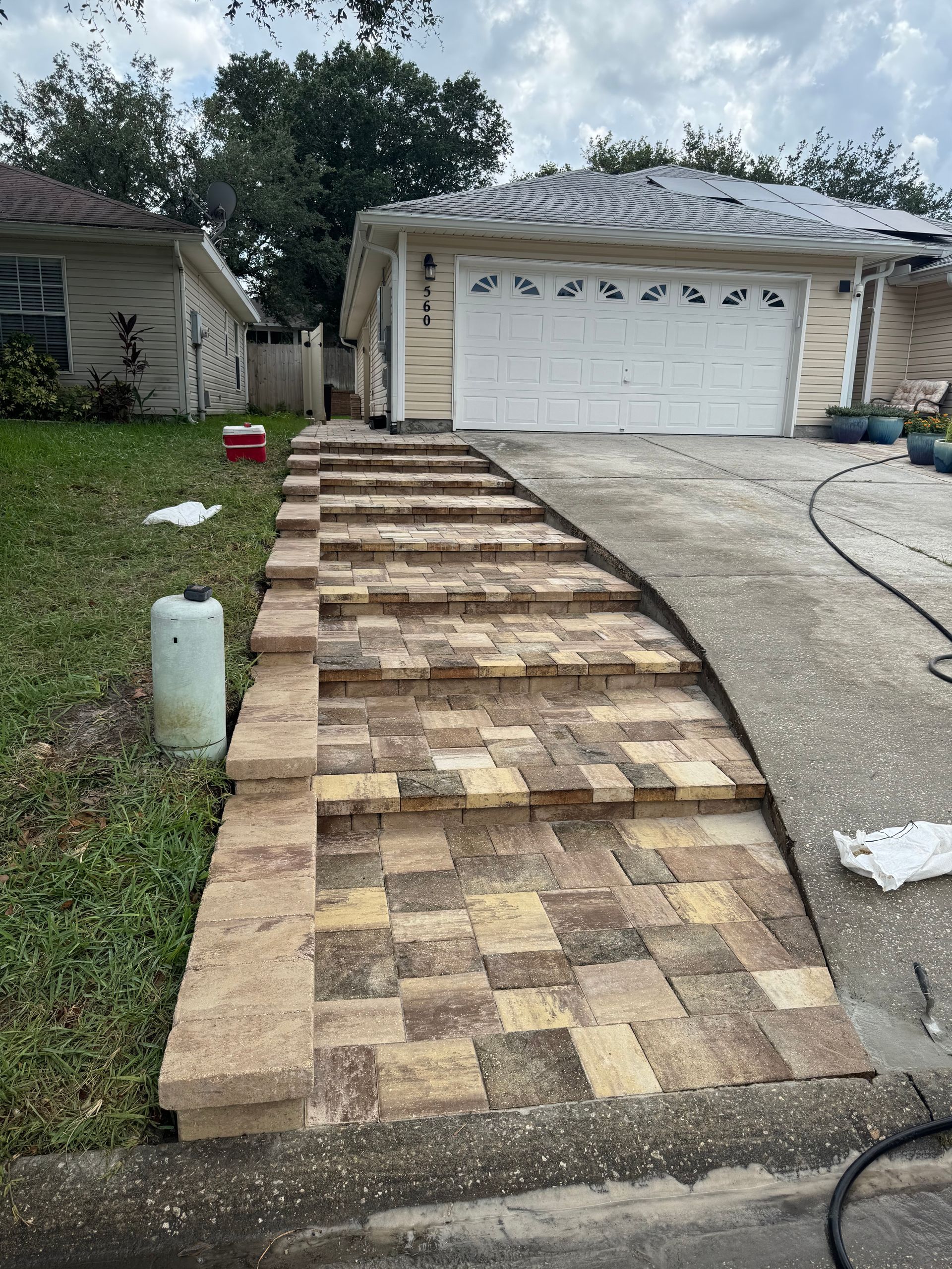 Brick pathway and steps leading to a house with a garage; a concrete driveway is adjacent.