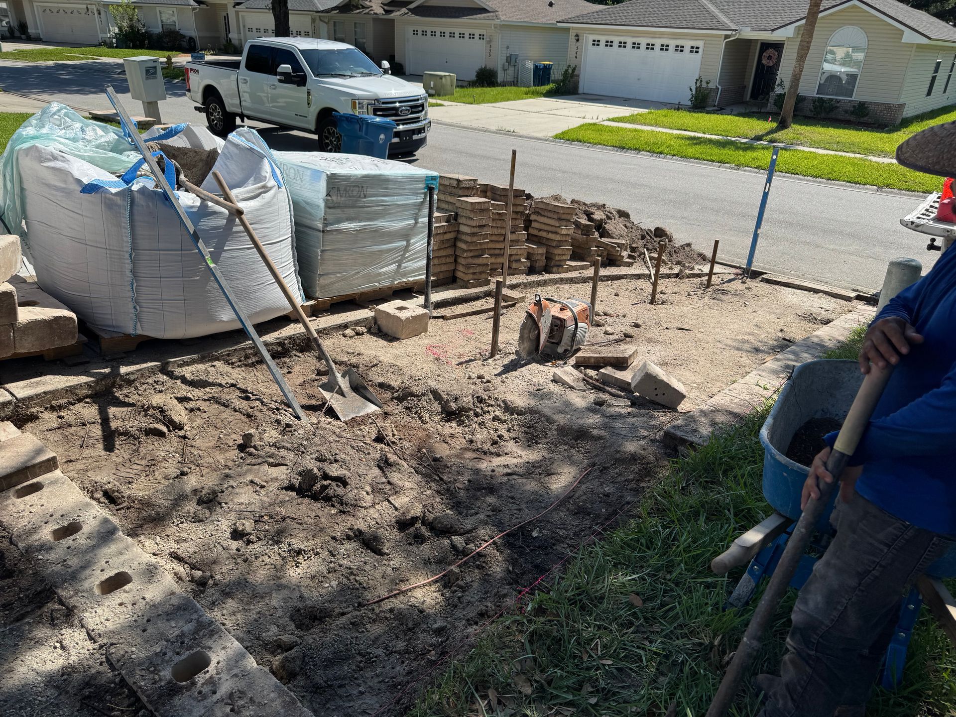 Construction site: workers preparing ground for a brick patio; materials include bricks, sand, and tools.