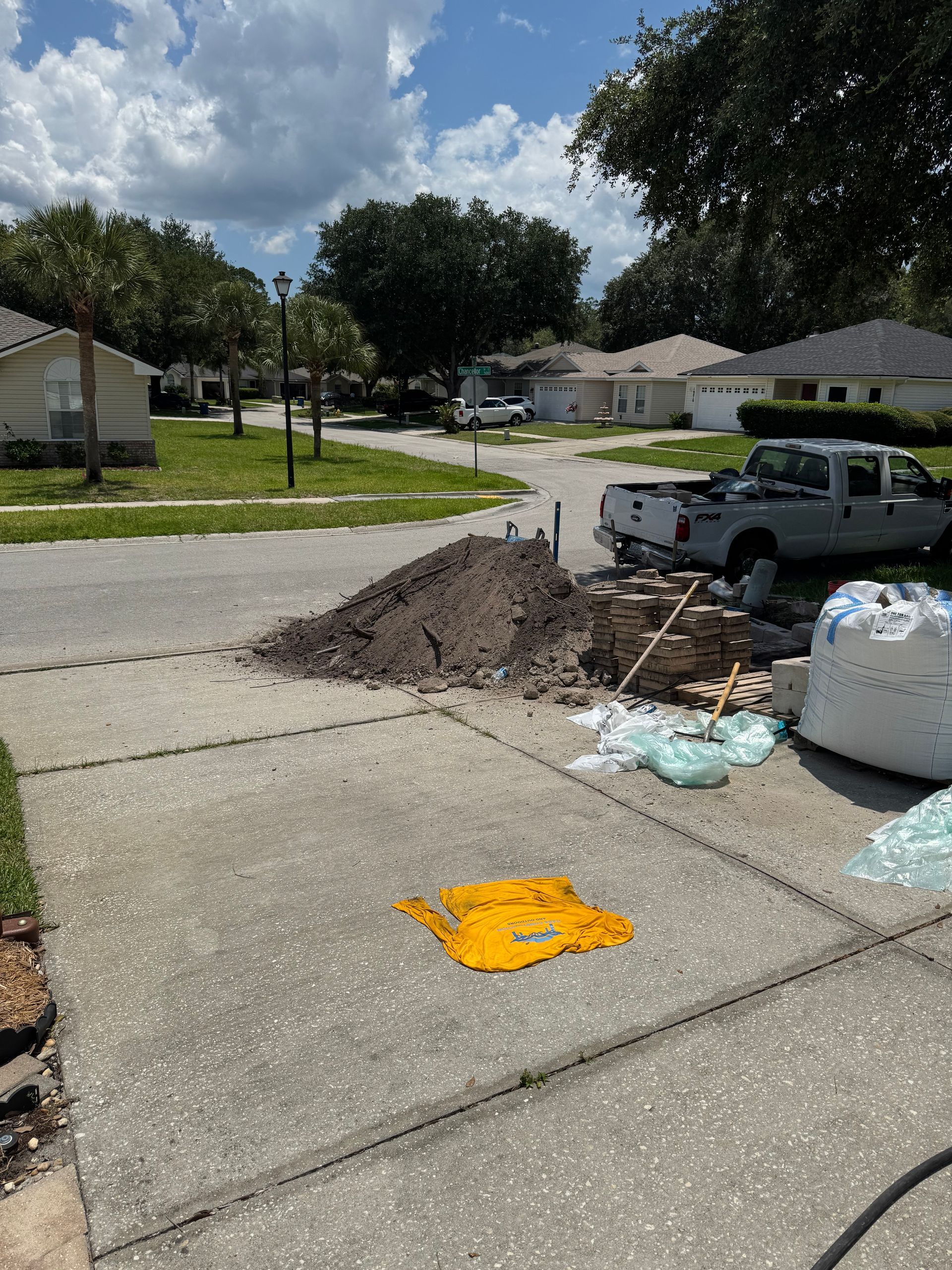 Construction site on a residential street. Pile of dirt, materials, and a pickup truck on the driveway. Sunny day.