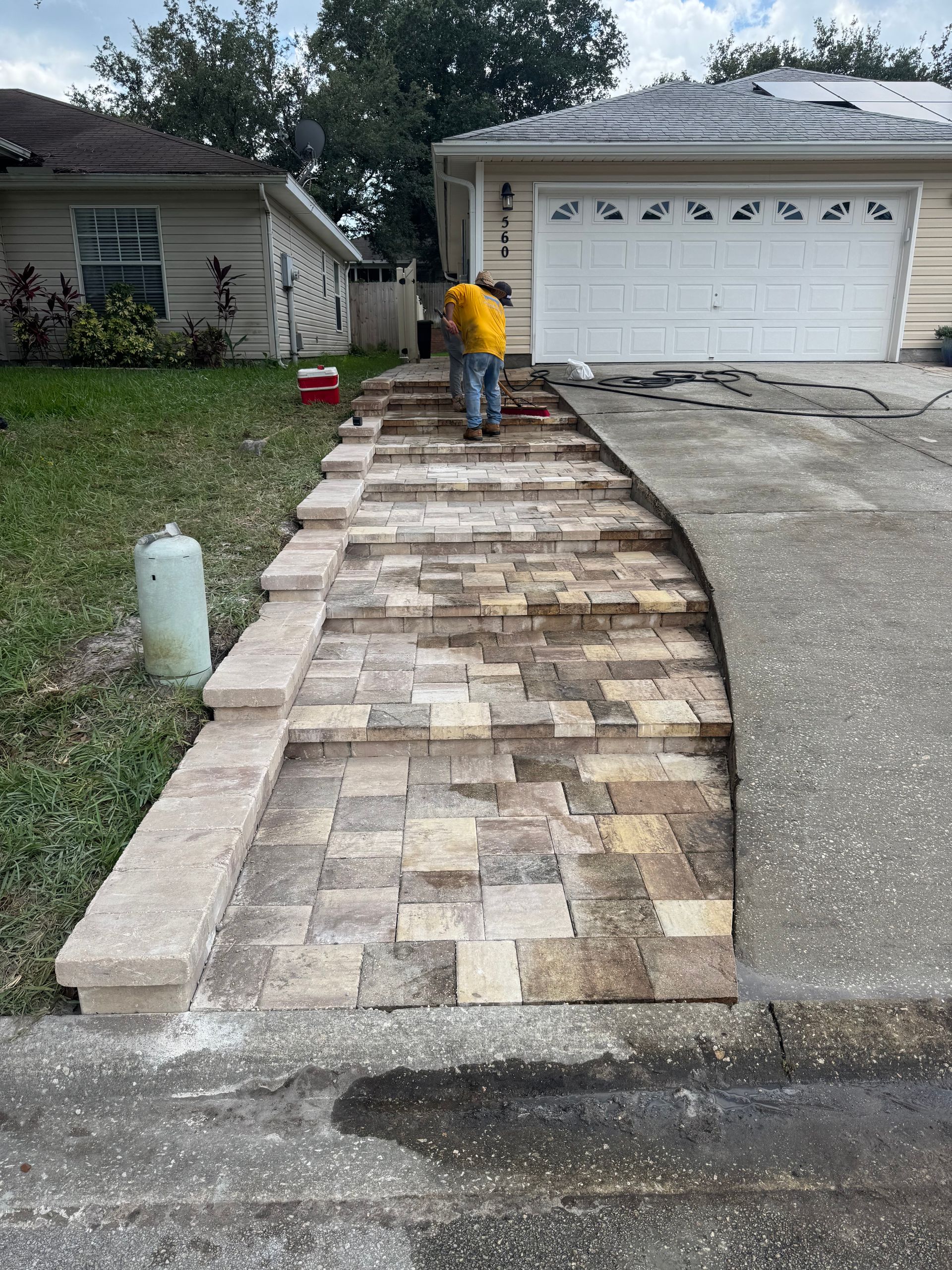 A person working on a brick pathway leading to a garage door. Cement driveway on right.