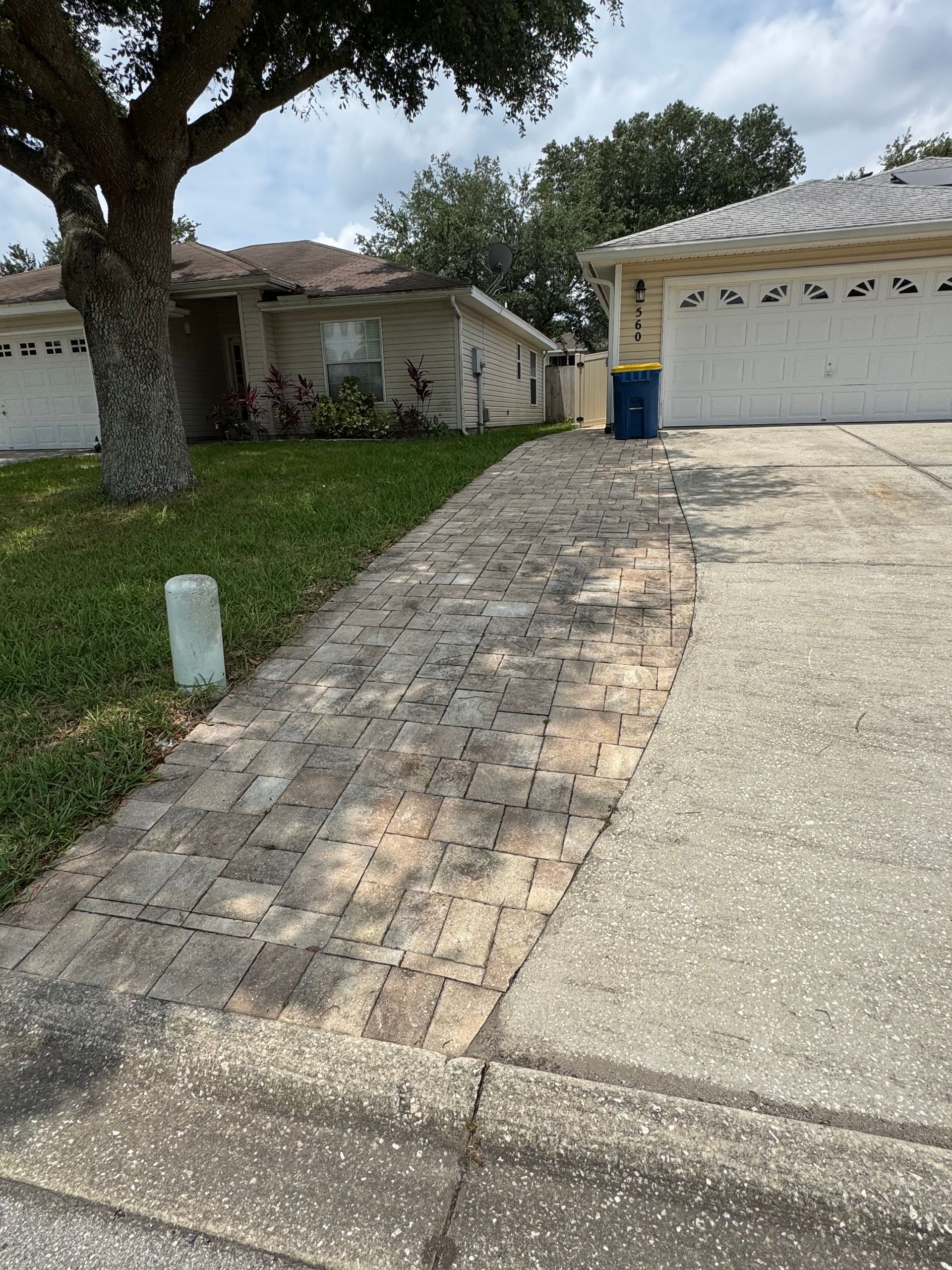 Brick pathway curving from driveway to a house with a garage; a tree on the left.