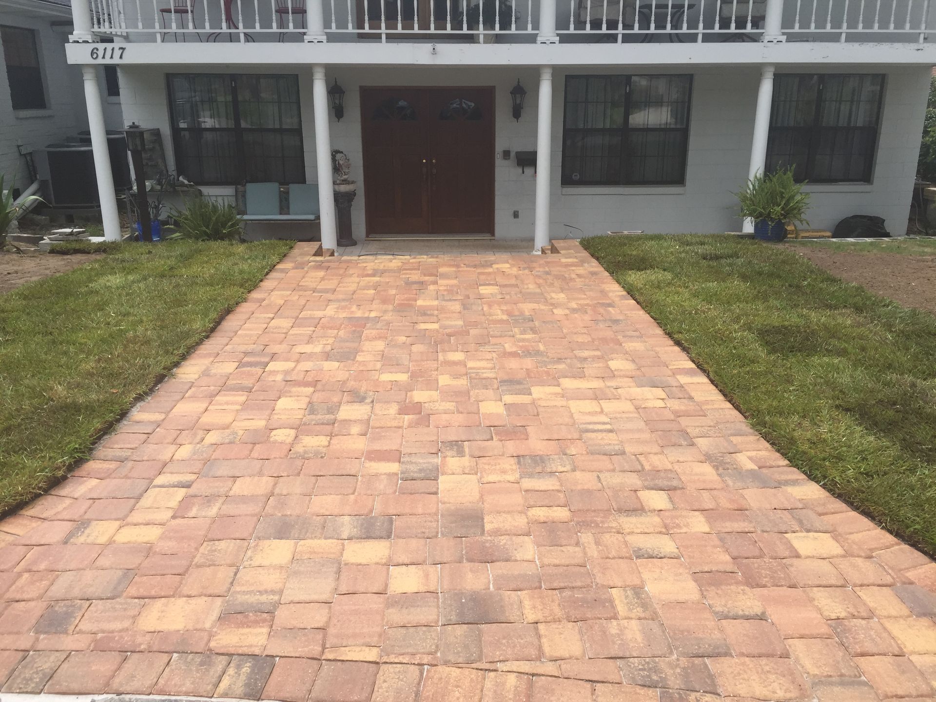 Brick paver walkway leading to a two-story house with green grass on either side.