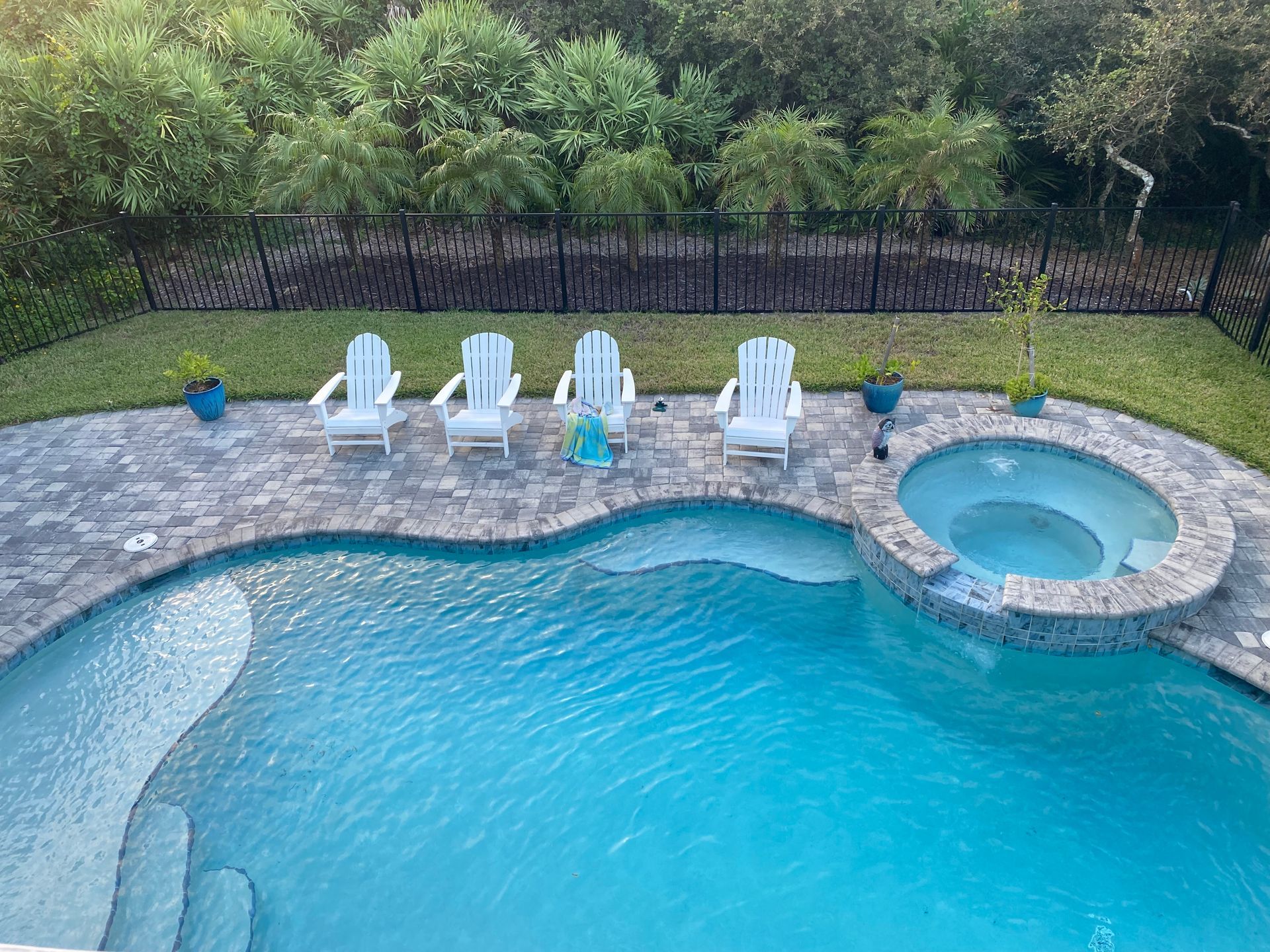 Swimming pool and hot tub with lounge chairs on a brick patio. Green lawn and trees in the background.