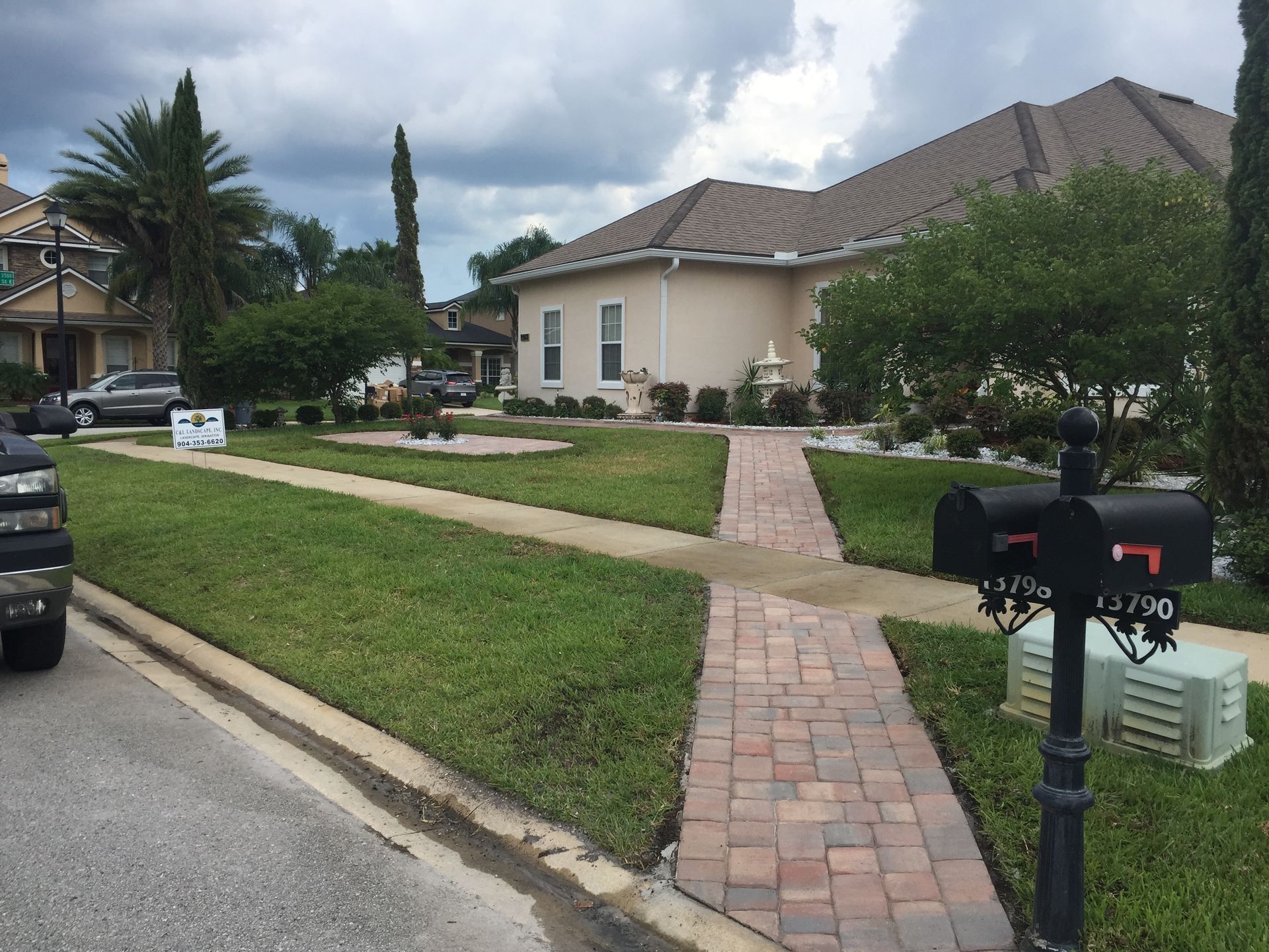 Brick walkway leading to a beige house with a mailbox, green lawn, and cloudy sky.
