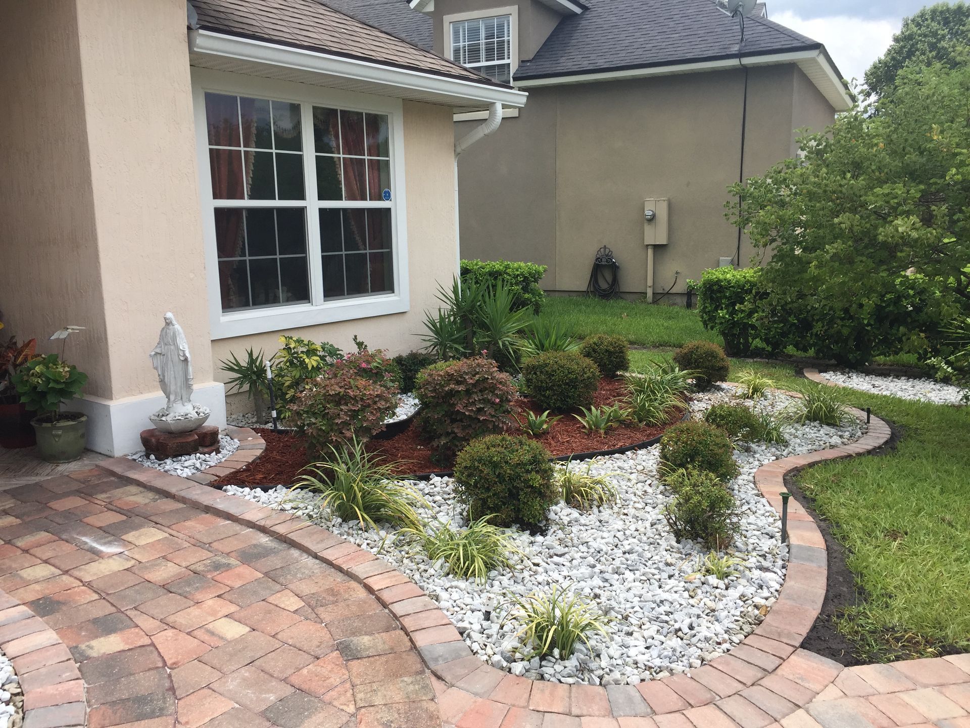 Landscaped front yard with brick walkway, beige house, and white rock border.