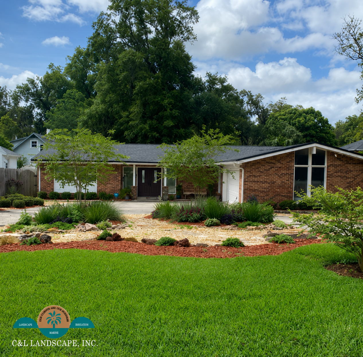 A single-story brick house with landscaping. Trees and grass in the yard, a blue sky overhead.