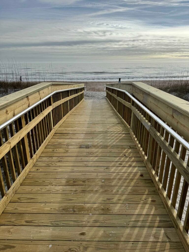 Wooden boardwalk leading to a beach and ocean under a cloudy sky.