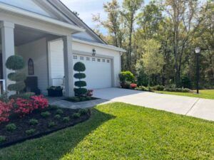 House exterior with manicured landscaping, garage, driveway, and trees in background.
