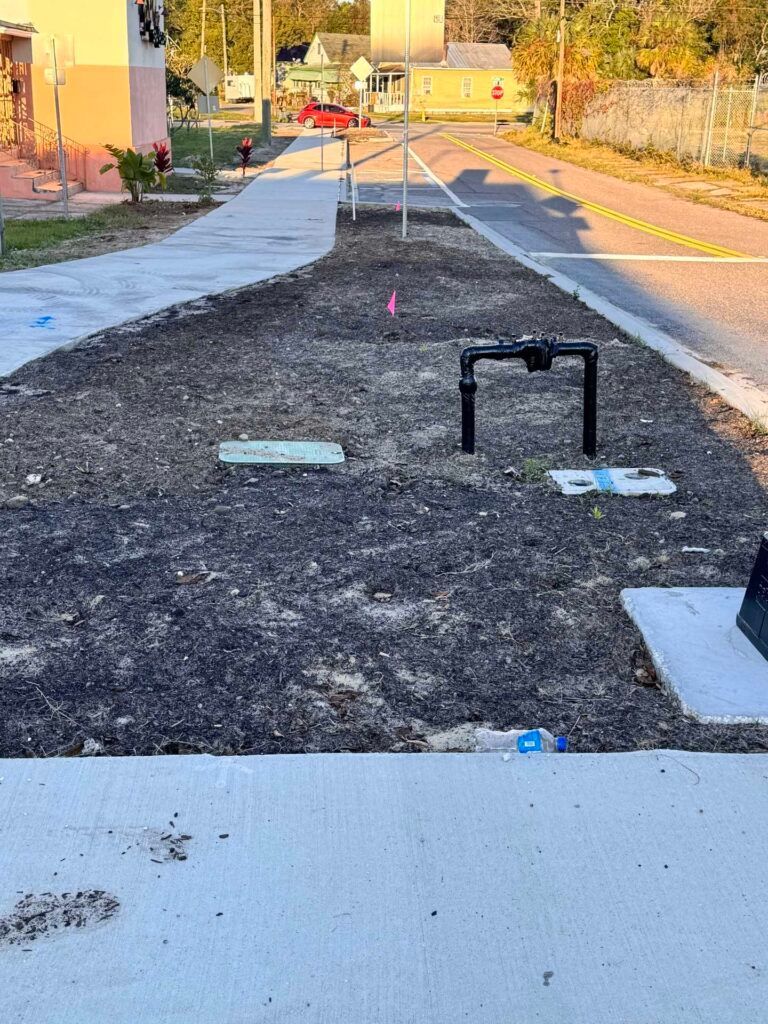 A street scene shows a newly planted median strip with utility boxes and a sidewalk.