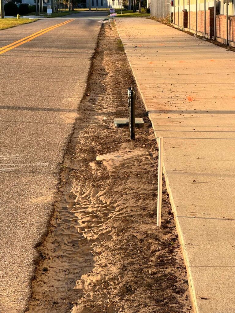 Road and sidewalk construction; trench dug between asphalt and concrete.