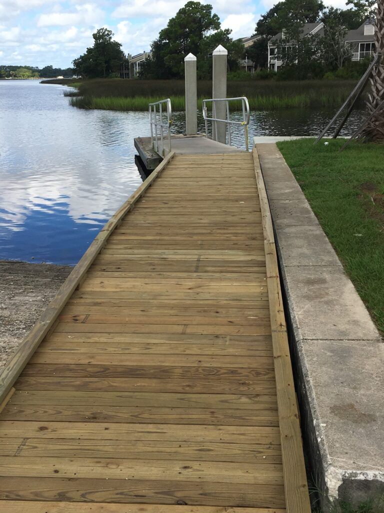 Wooden dock leading to a calm lakeside with houses and trees in the background