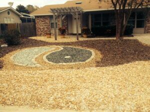 A home's front yard features a decorative gravel design resembling a yin-yang symbol.