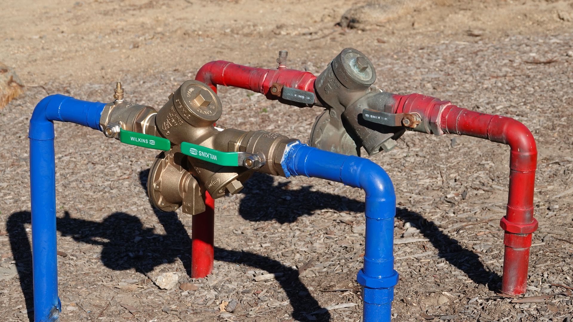 Blue and red industrial pipes and valves on dry ground outdoors