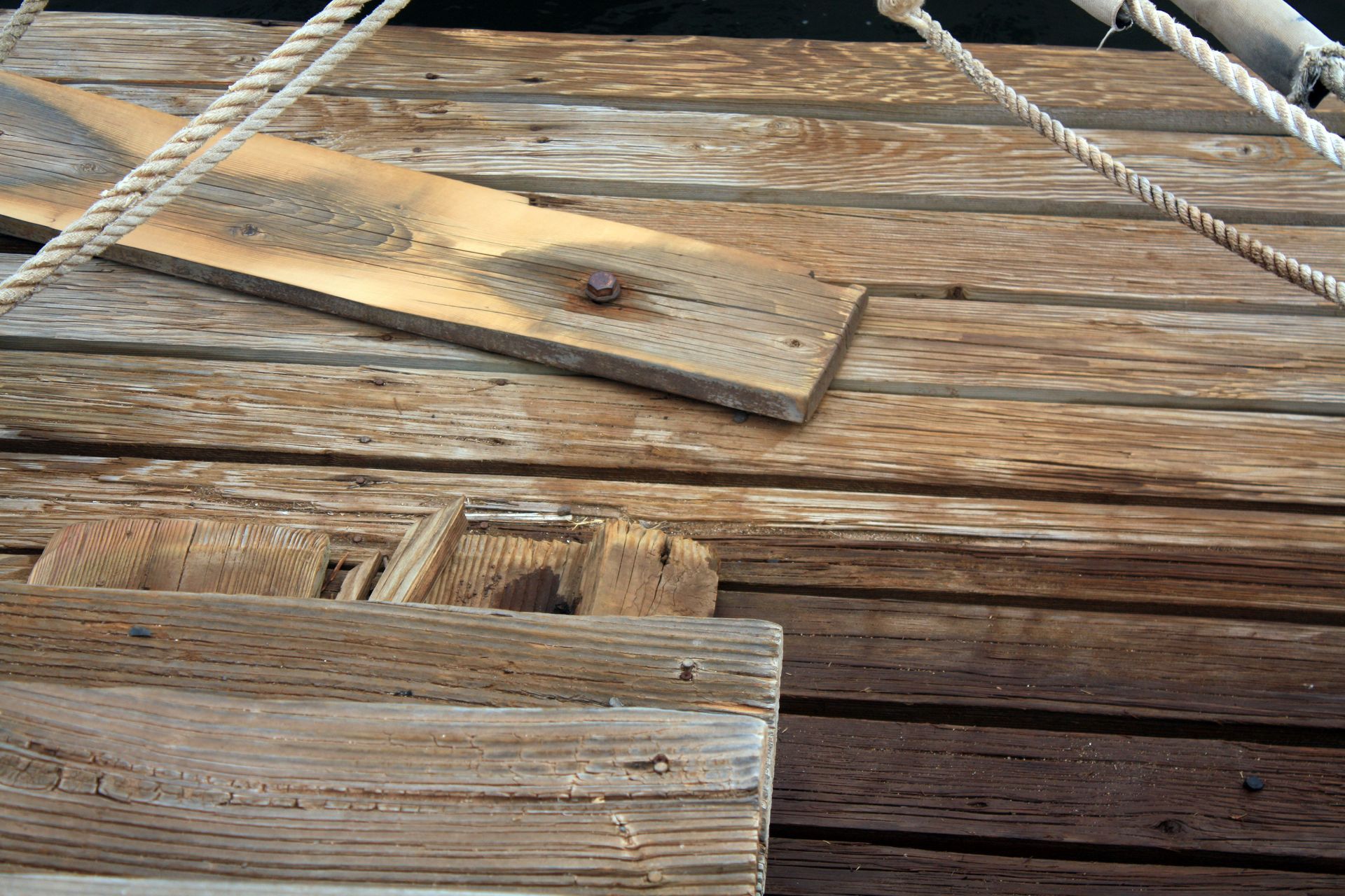 Weathered wooden boat deck with rope lines and a plank across the boards