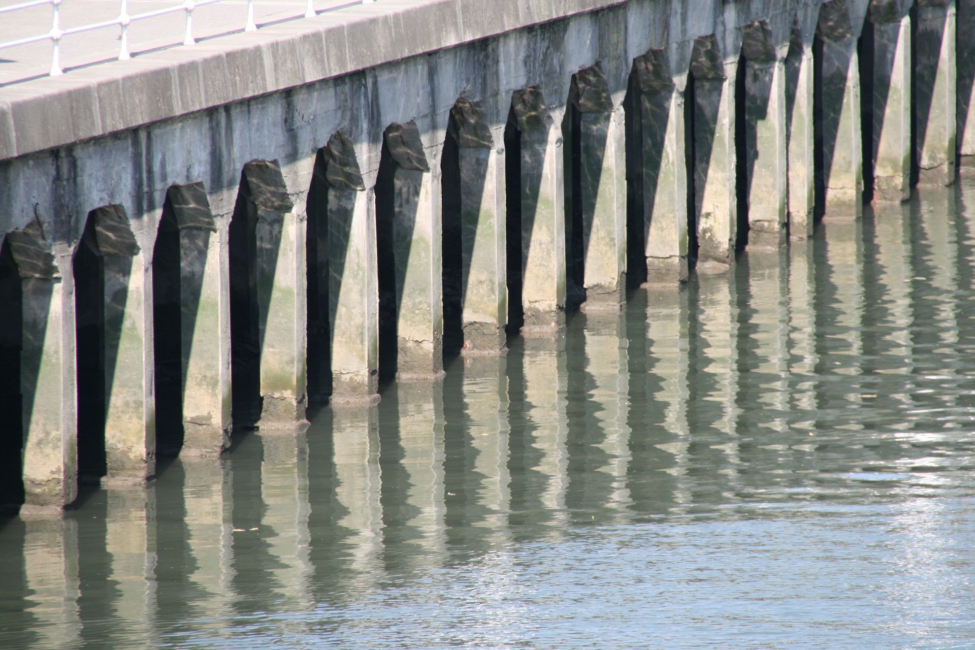 Weathered black pilings along a waterfront wall, reflected in calm water