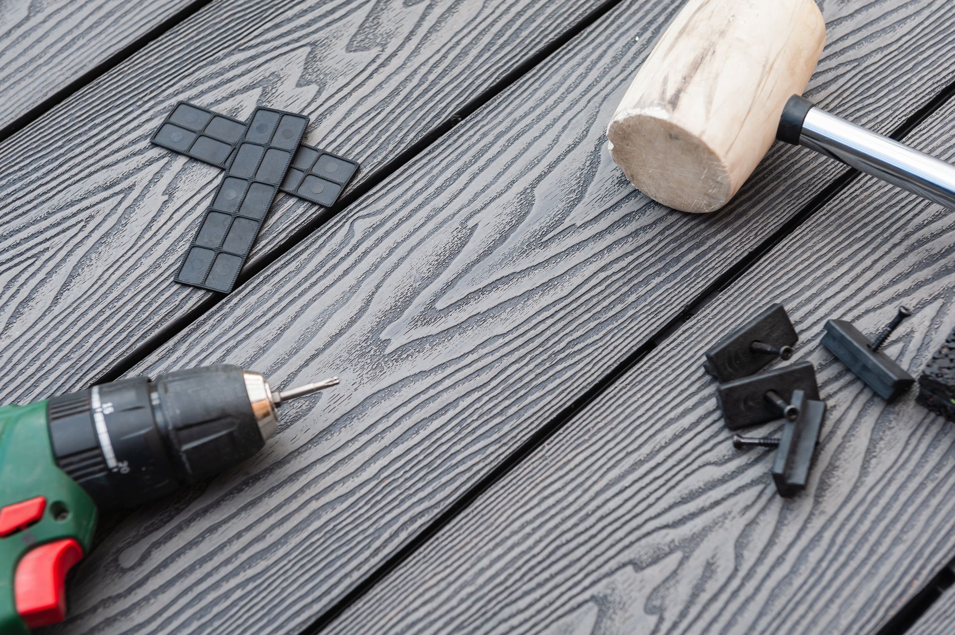 Roofing tools and black shingles on a gray roof, with a drill, mallet, and clips.