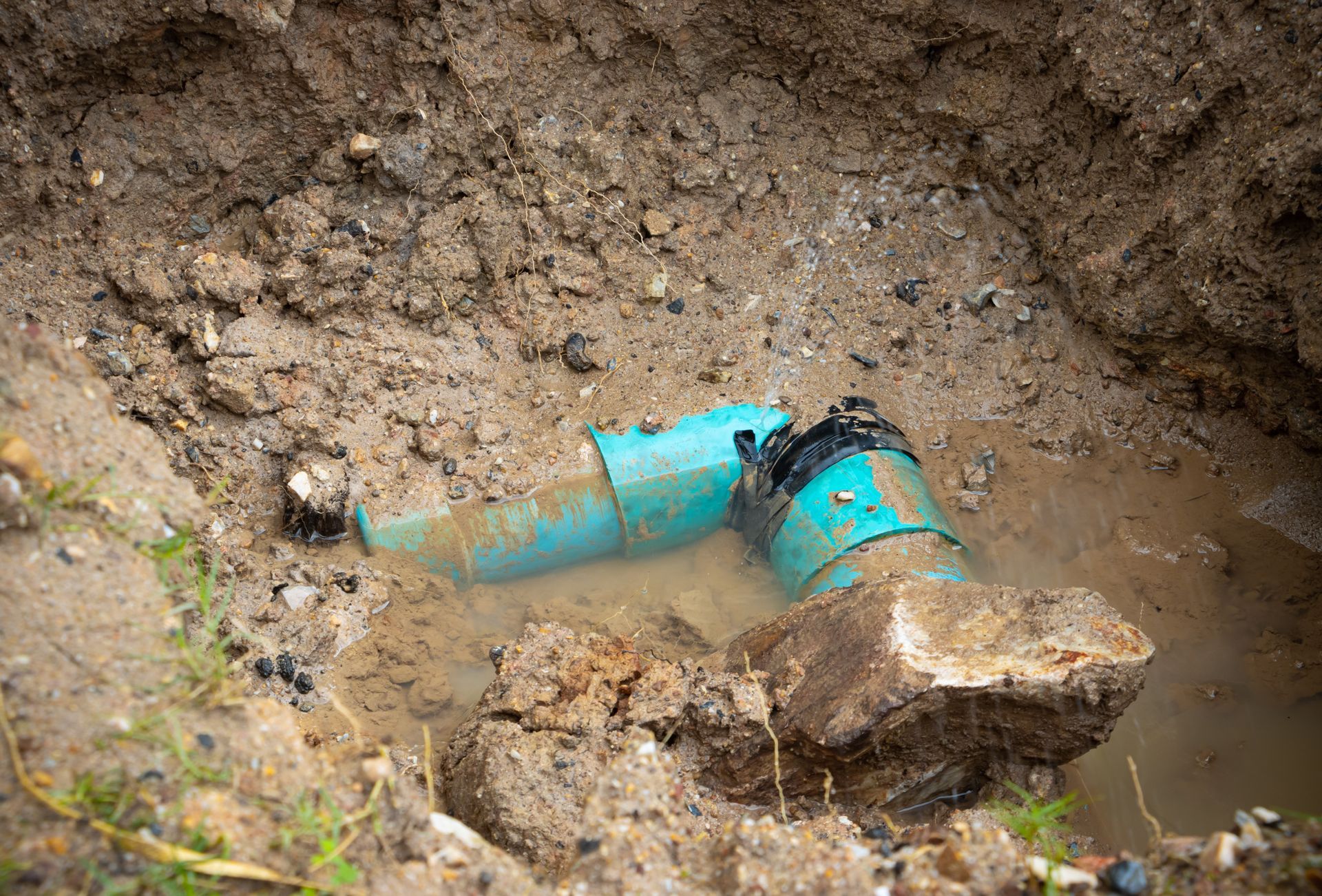Broken blue pipe leaking muddy water in a dirt trench