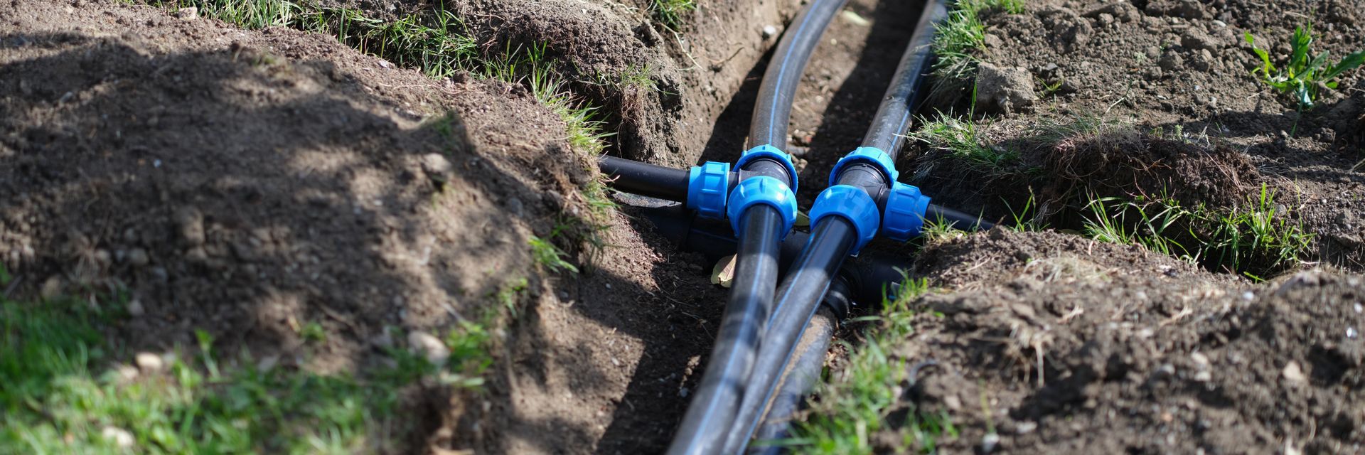 Black irrigation pipes with blue couplings running through a dirt field trench