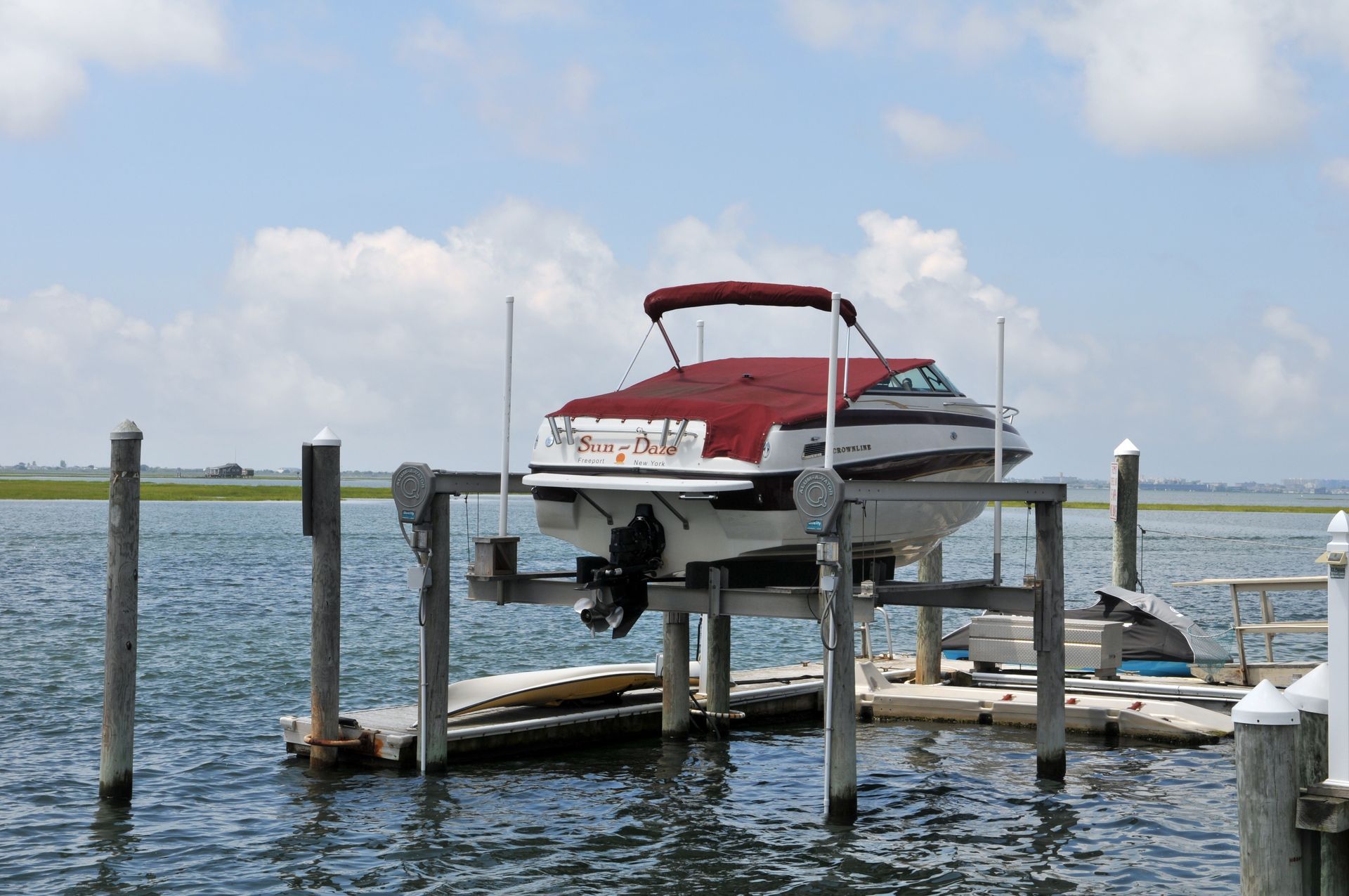 Red-and-white motorboat docked at a wooden pier on a calm waterfront under a cloudy sky