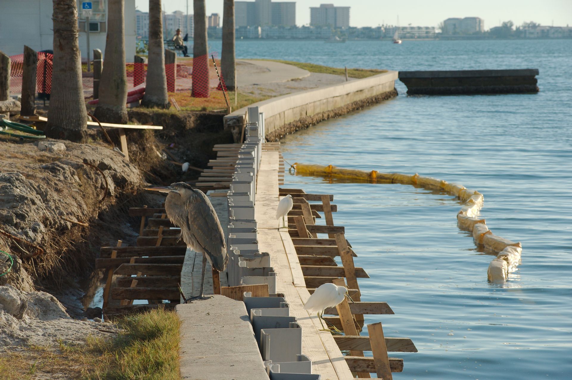 Damaged seaside walkway with a collapsed retaining wall along calm blue water