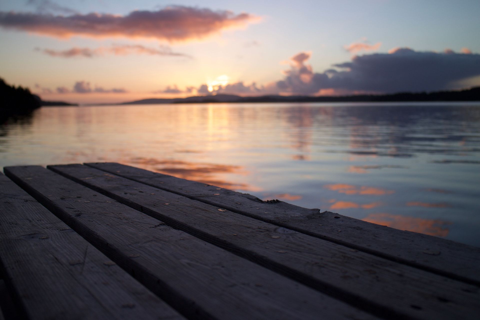 Wooden dock at sunset over a calm lake, with colorful clouds reflecting on the water.