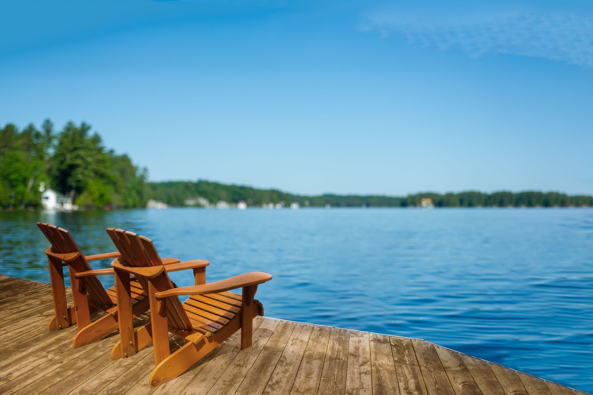 Two wooden chairs on a dock overlooking a calm blue lake and tree-lined shore