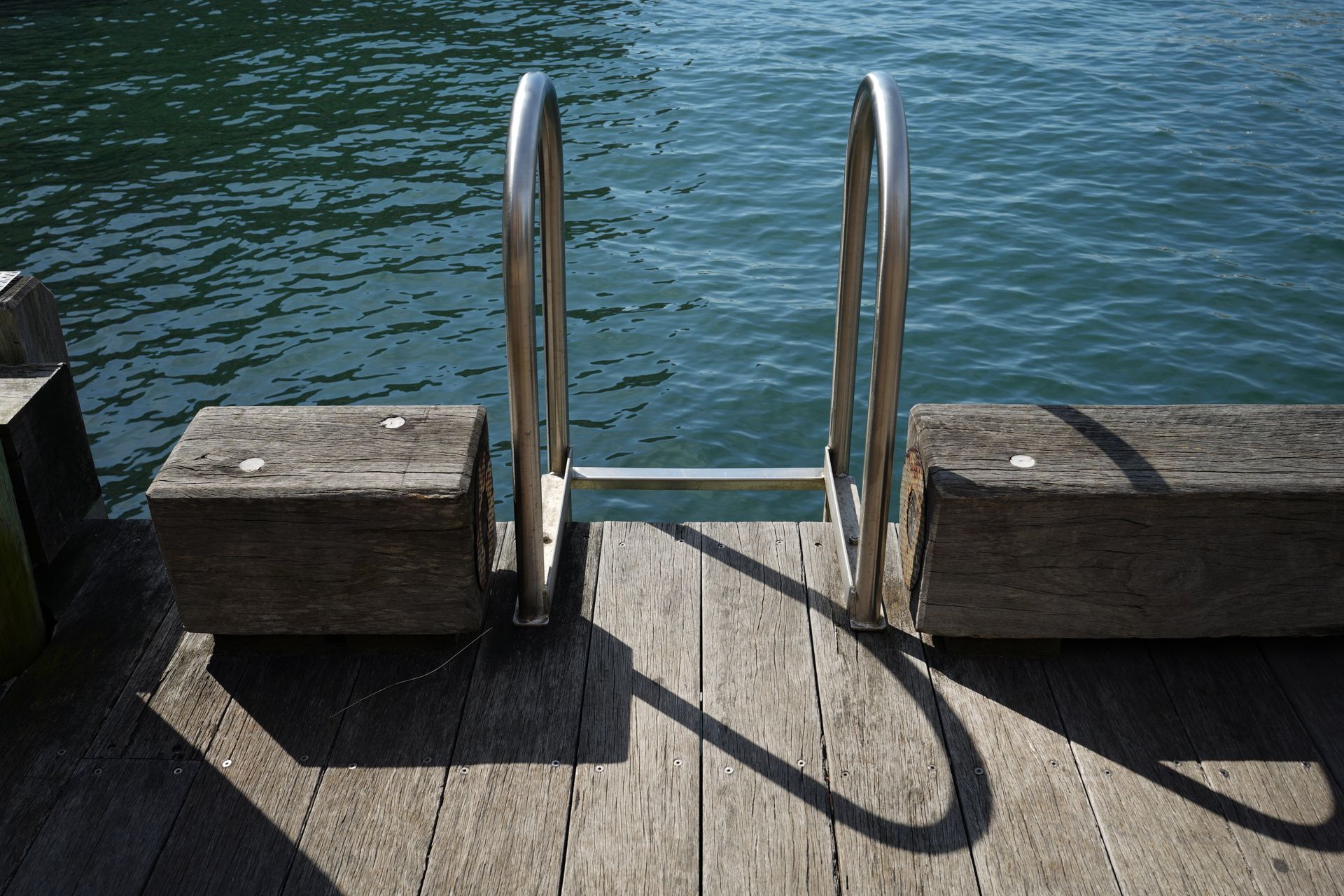 Dock ladder descending into blue water beside weathered wooden planks
