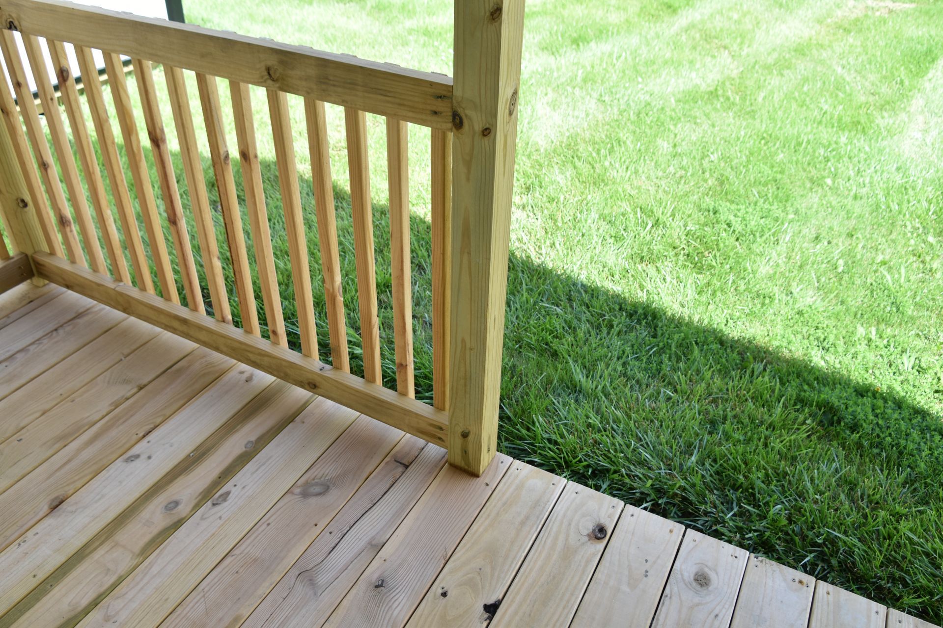 Wooden porch deck with railing beside a green lawn