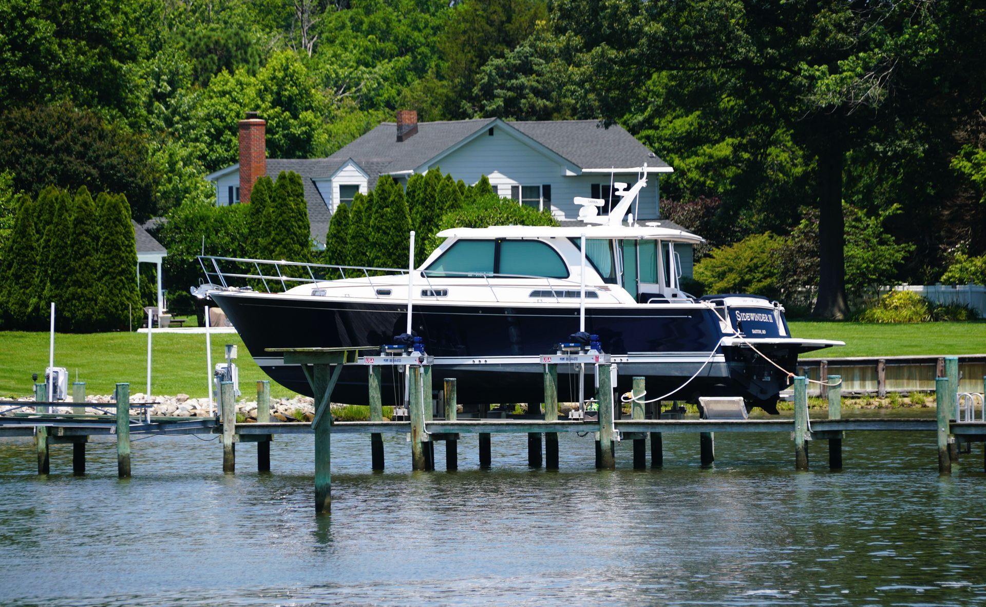 White motor yacht docked on a lake beside a house and green shoreline.